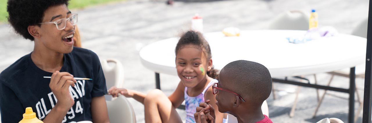 Summer camp with kids outside smiling at white tables